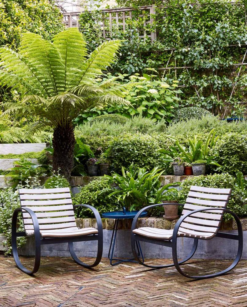 Two wooden outdoor chairs on a stone herringbone patio.