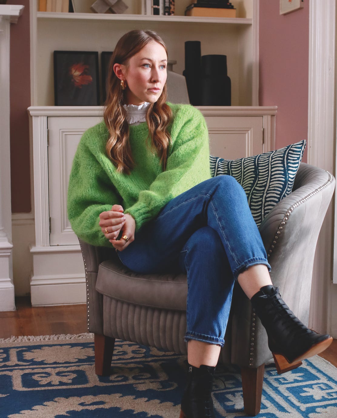 Erin Doherty wearing a green jumper, sitting in an Ash Grey Crosby armchair