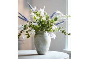 A vase with a large bouquet of faux blue and white flowers on top of a table.