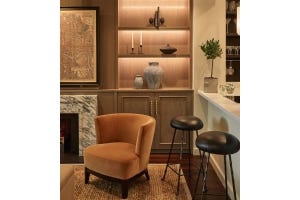 A cosy corner featuring an orange velvet armchair, a bookcase with integrated lighting and a kitchen counter with bar stools.