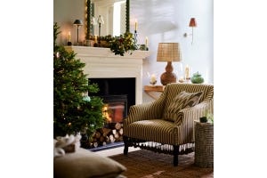 A green-and-white striped armchair sits in front of a roaring fire and a Christmas tree