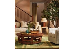 A softly coloured bedroom with a fourposter bed, floral-print red, olive green and cream armchair, bedspread and rug.