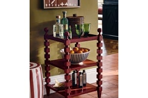 A red side table with cubed, bobbin-inspired legs holds an array of glassware and bottles of drink.