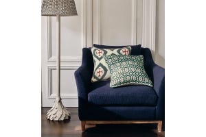 A navy blue armchair, decorated with patterned pillows, sits next to a white floor lamp featuring a patterned shade.