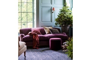 A bright magenta velvet sofa sits in a blue-walled room. A Christmas tree is seen in the background, and the sofa is decorated with pillows.