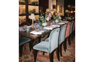 A row of blue and red velvet dining chairs arranged around a rectangular dining table, with the table set with patterned tableware and flowers.