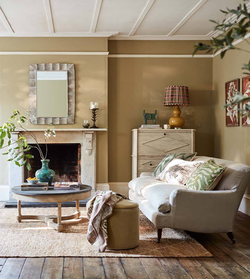 A summery sitting room with ochre walls, a linen sofa and green cushions.