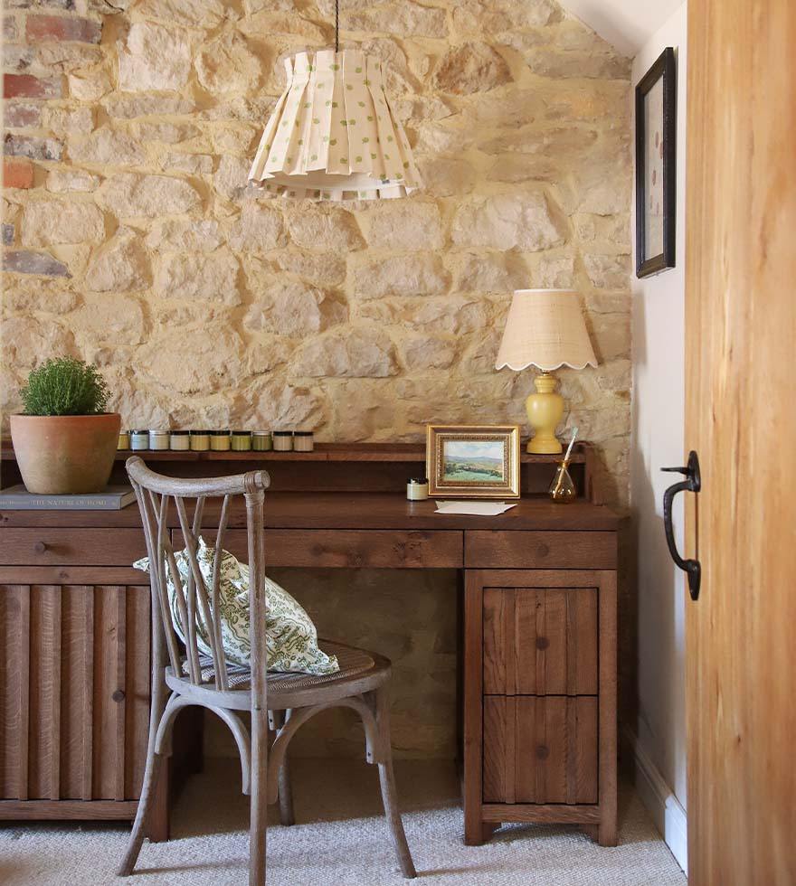 A wooden desk and chair sitting against an exposed brick wall.