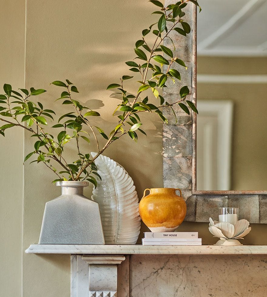 An array of decorative home accents and a vase with long faux stems on top of a mantlepiece. A large mirror hung on the wall behind.