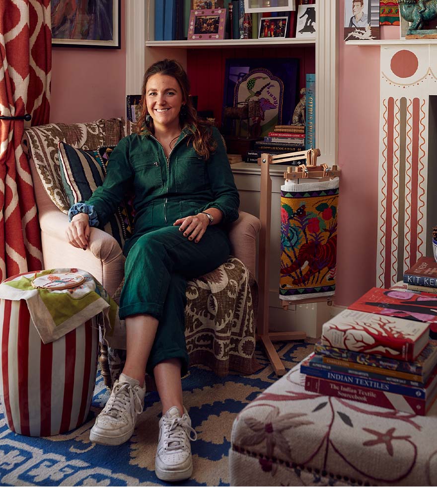 Eppie Thompson wearing a green jumpsuit and sat in an armchair in her pink, colourful sitting room