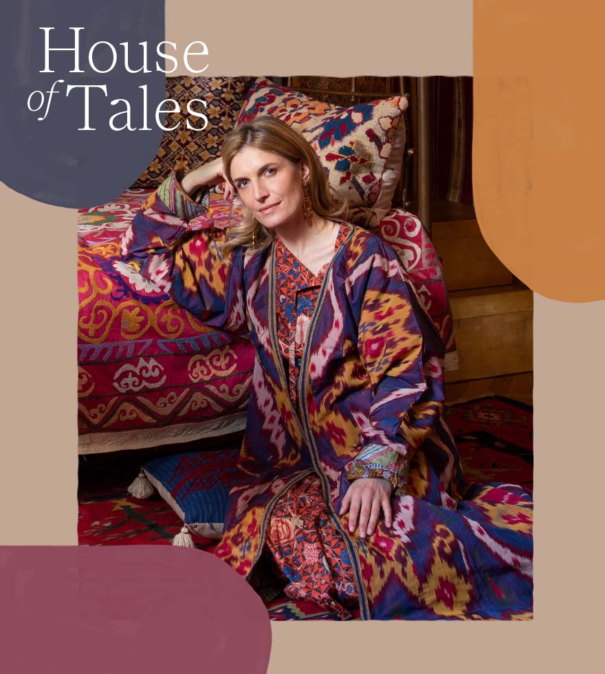 Martina Mondadori is sitting on the floor wearing a bright abstract patterned dress leaning with on a red patterned sofa.