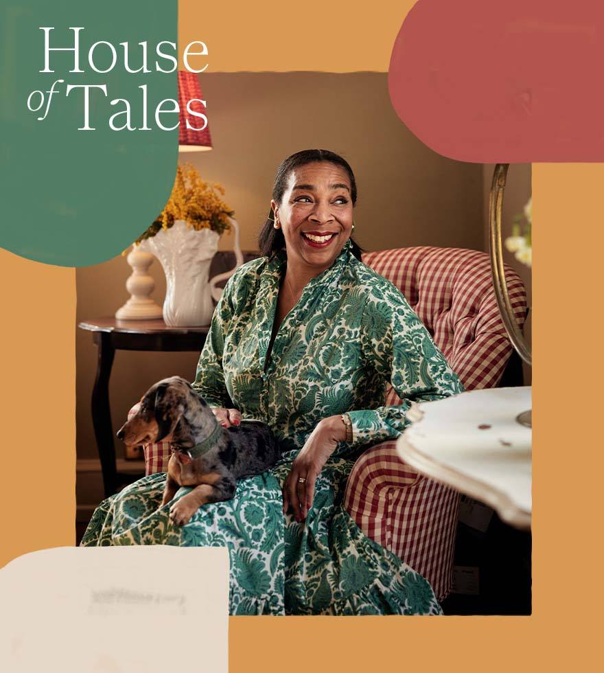 Paula Sutton is sitting in a red and white gingham chair with a small dog on her lap.