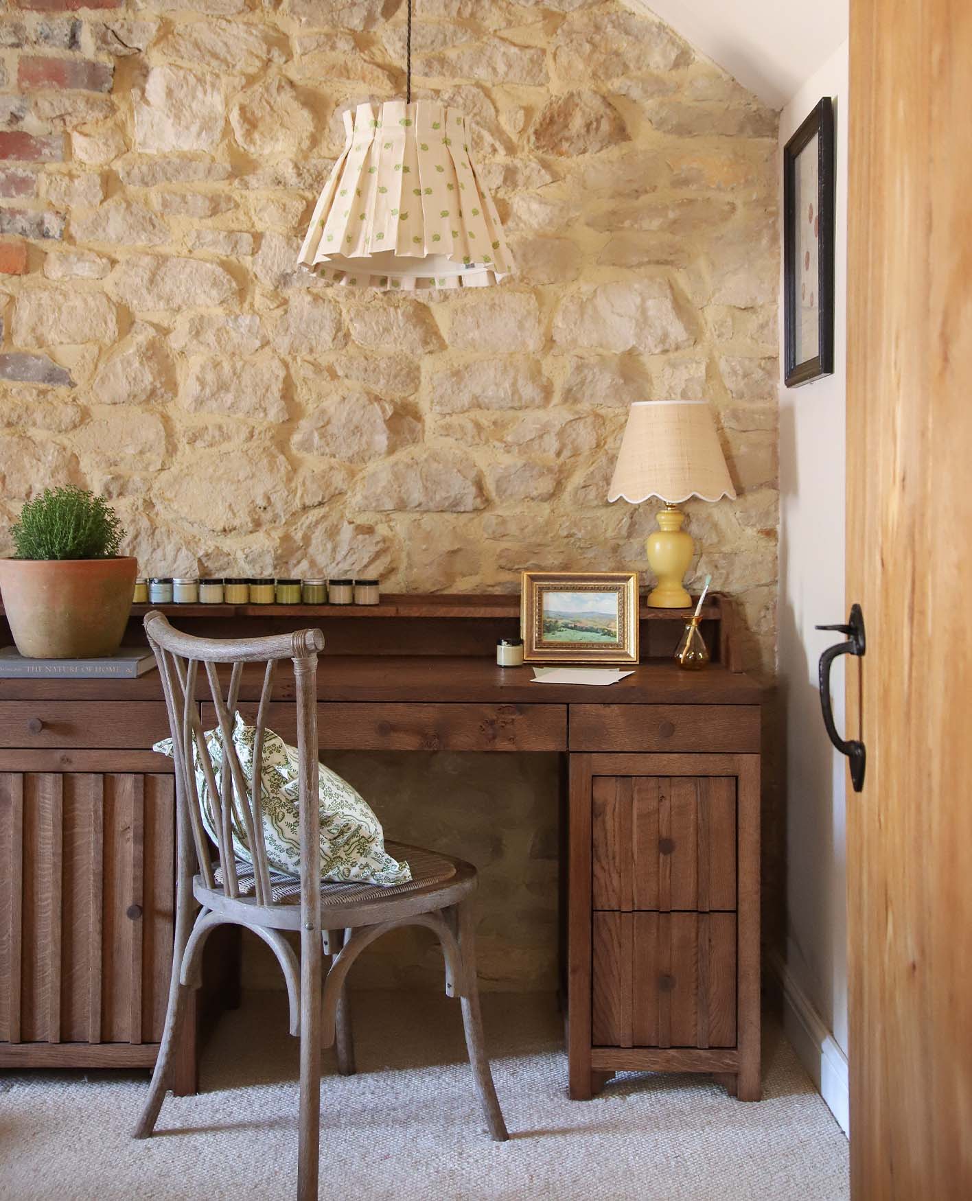 A wooden desk and chair sitting against an exposed brick wall.