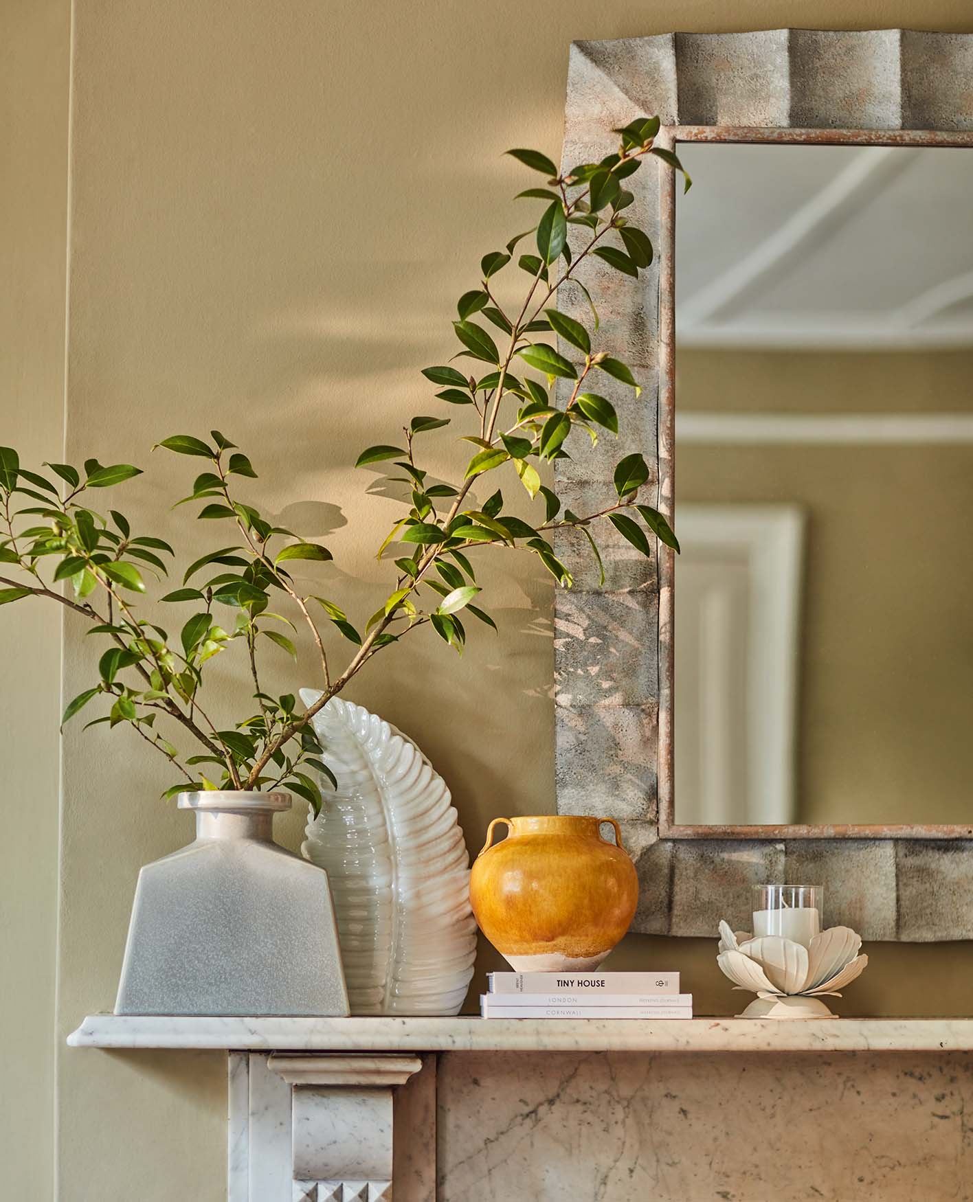 An array of decorative home accents and a vase with long faux stems on top of a mantlepiece. A large mirror hung on the wall behind.