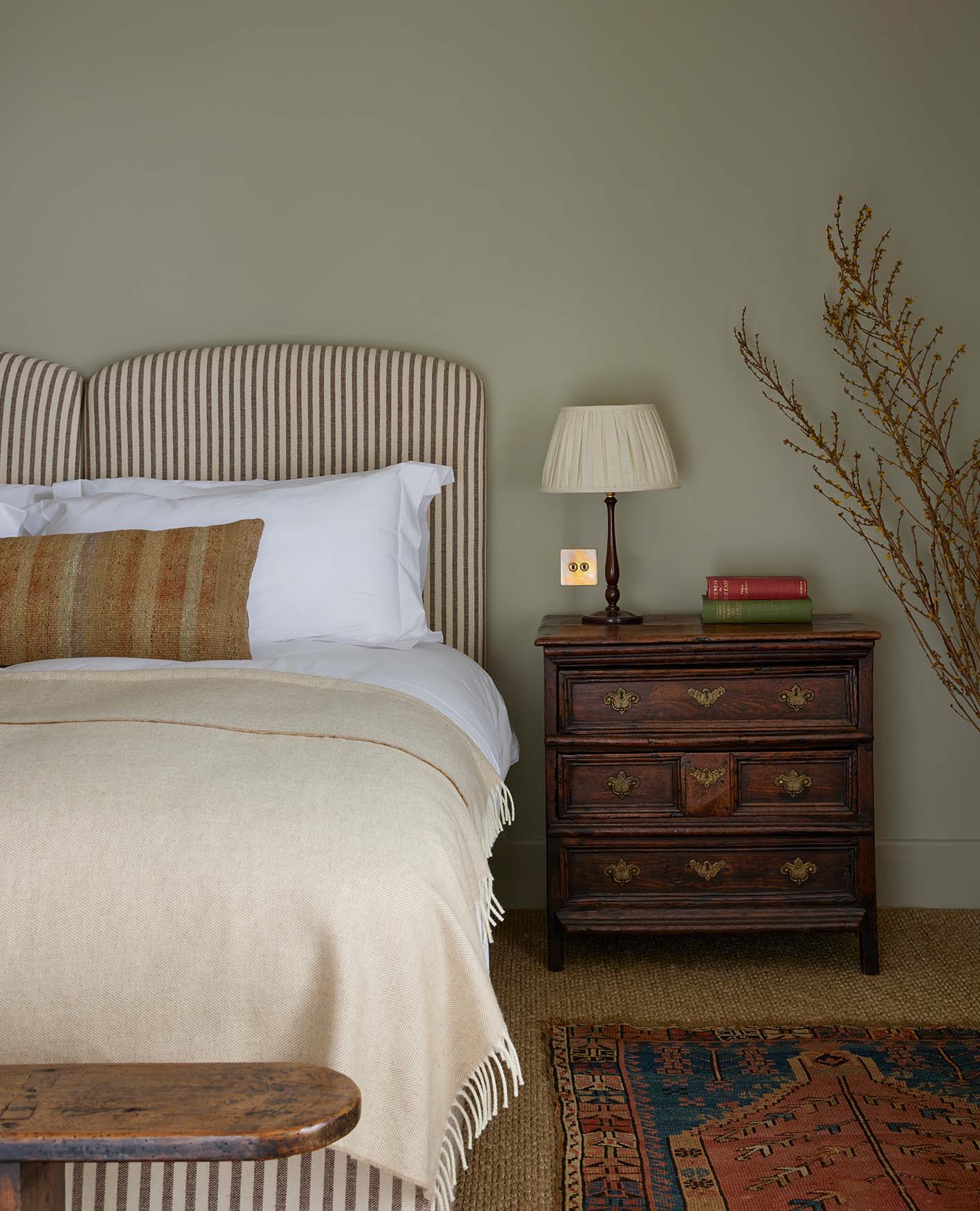 A double bed with a striped headboard with a cream throw and an orange stripe pillow. A dark wooden bedside table beside.