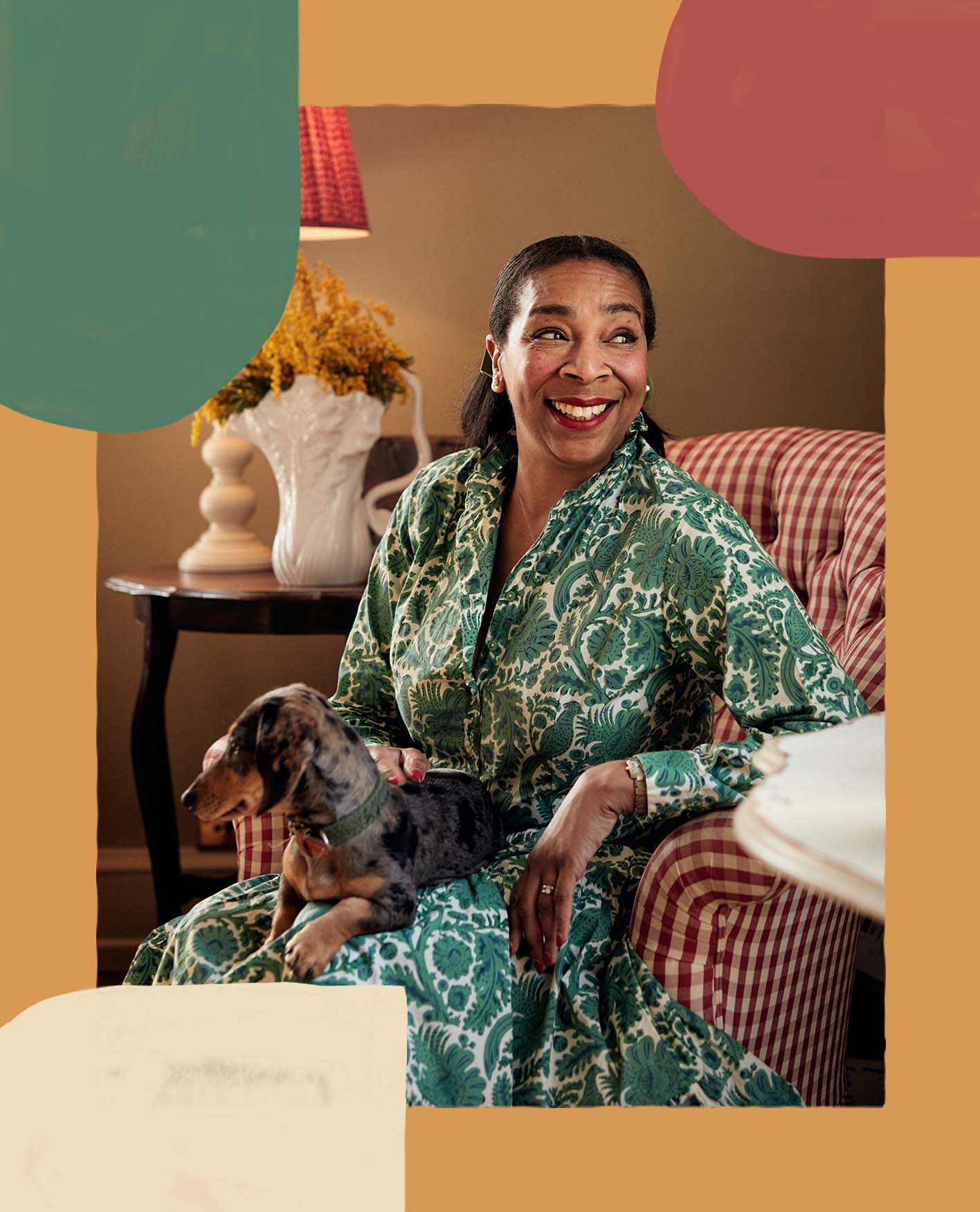 Paula Sutton is sitting in a red and white gingham chair with a small dog on her lap.