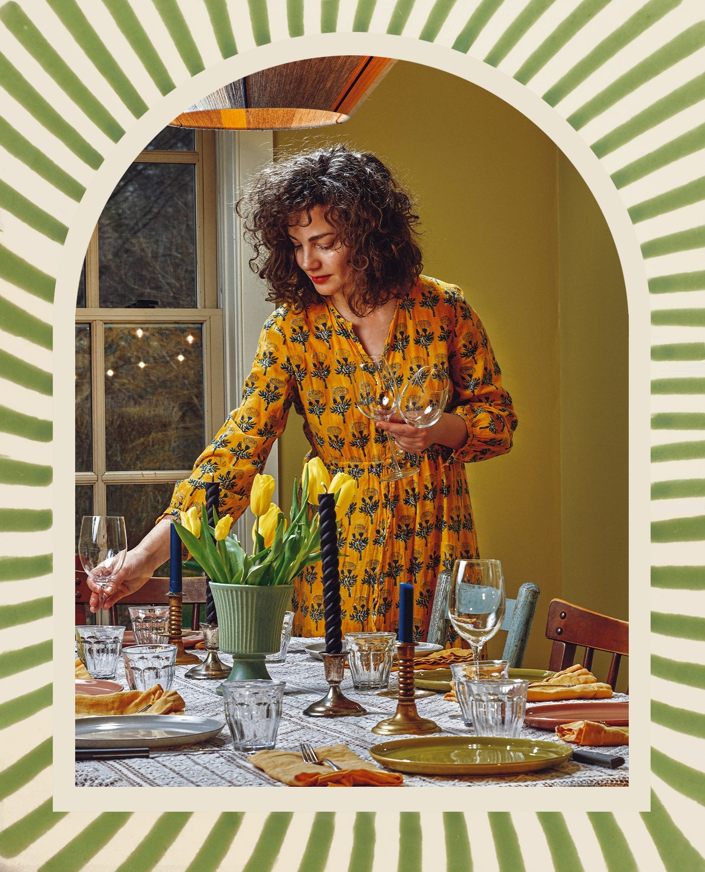 Food writer, Anna Stockwell, decorating a dining table, featuring candlesticks, glassware and crockery on a fabric tablecloth