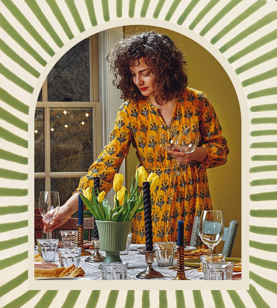 Food writer Anna Stockwell decorating a dining table, featuring candlesticks, glassware and crockery on a fabric tablecloth