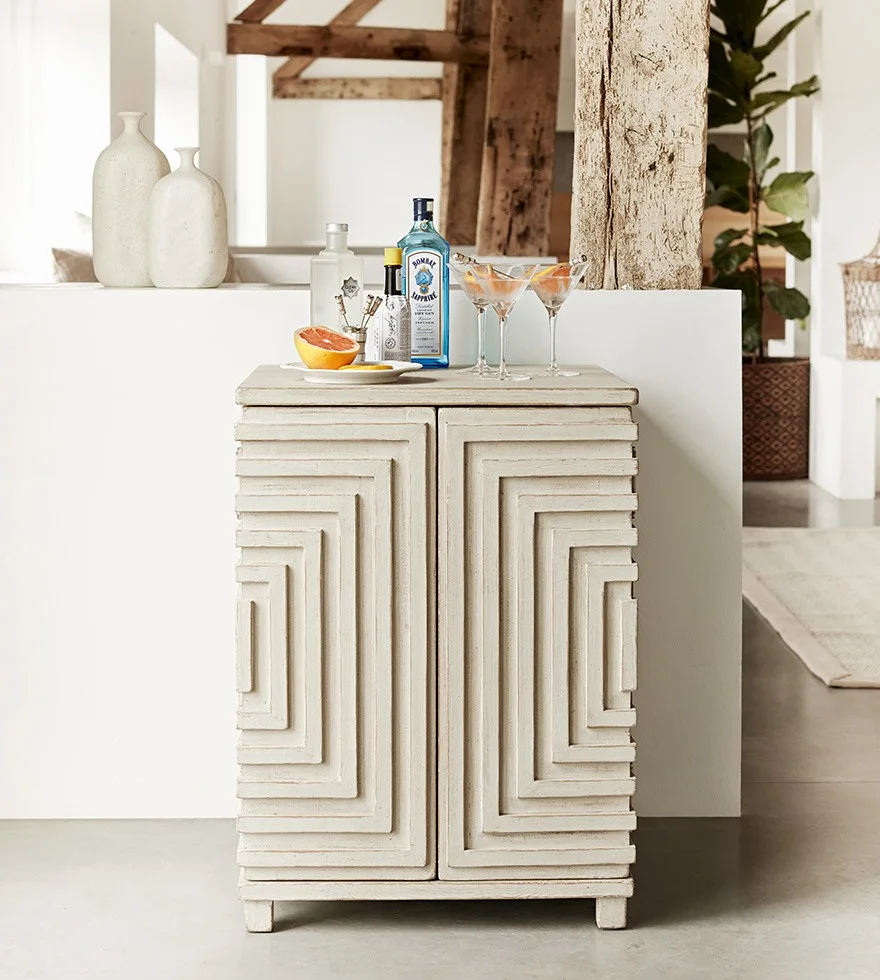 A white cabinet with cocktail glasses and drinks bottles on top