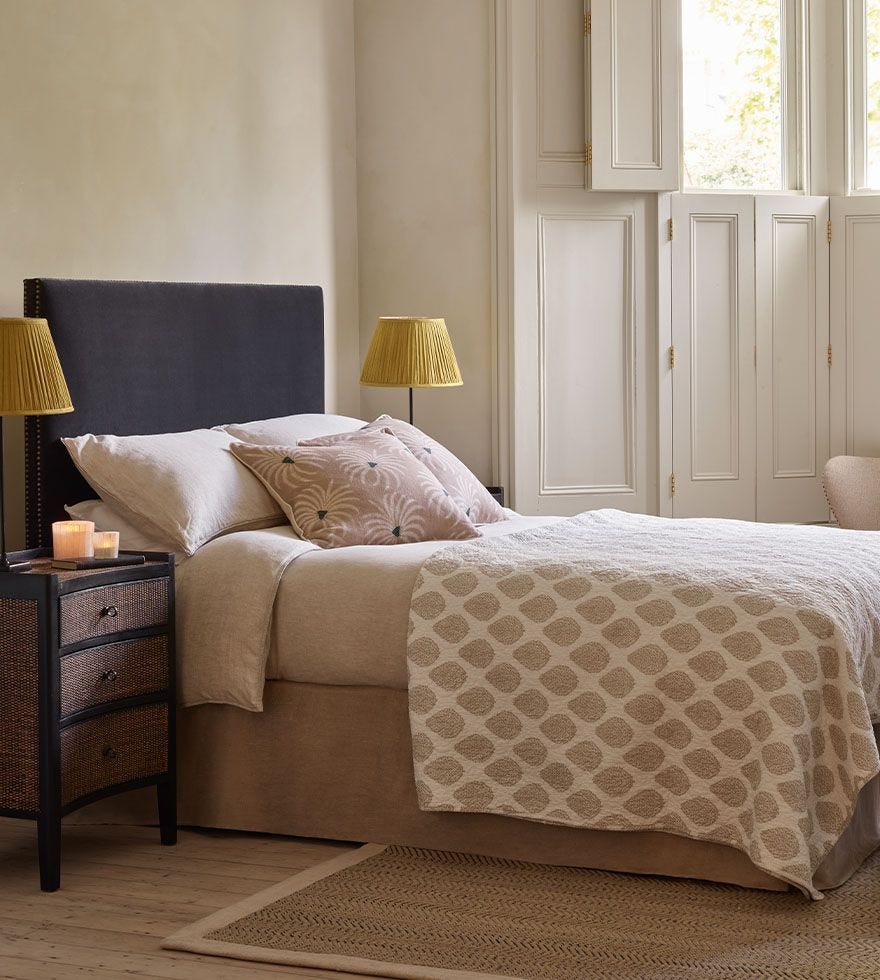 A cosy bedroom setting, featuring a navy blue headboard, patterned quilt and pillows and yellow pleated lampshades.