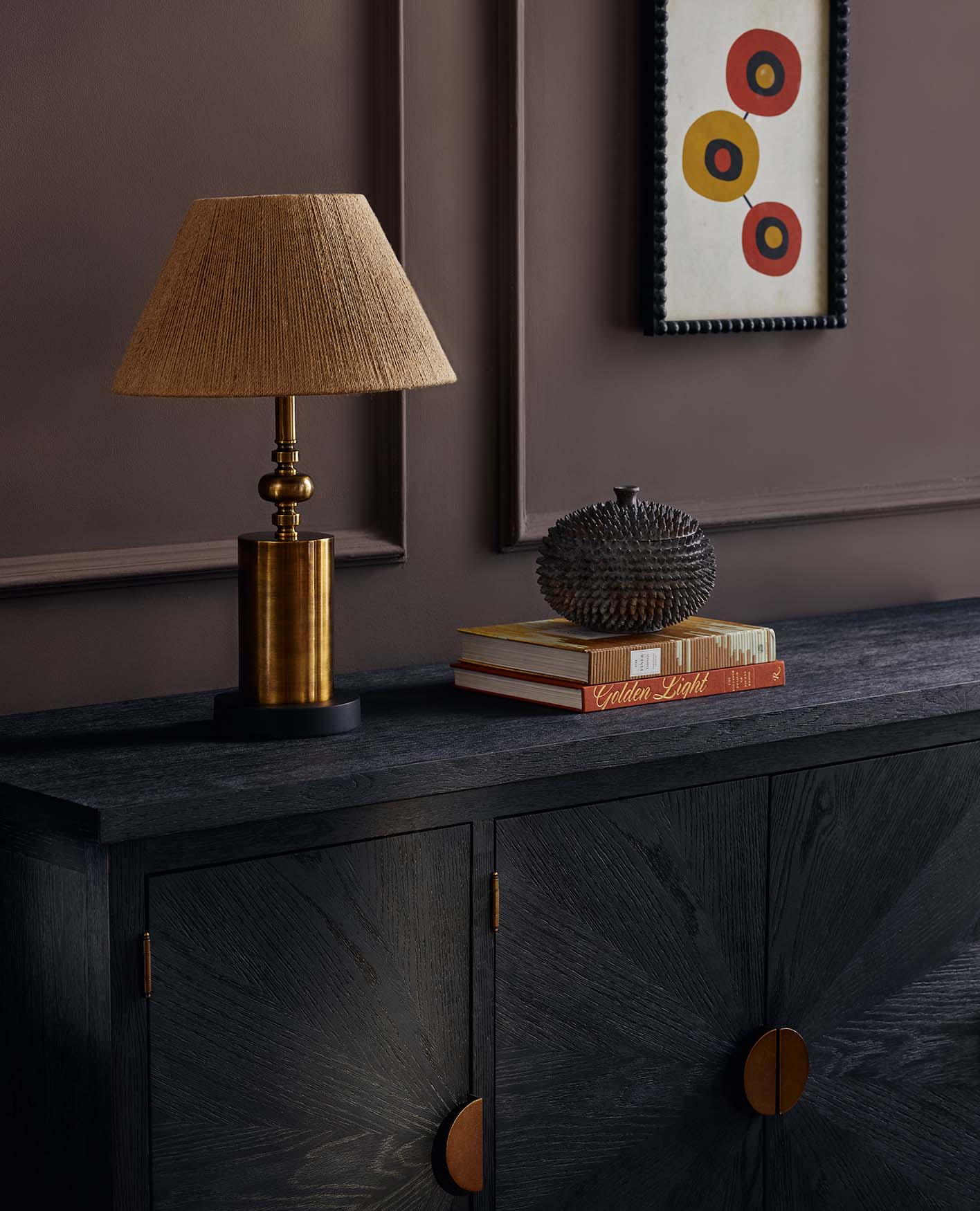 A dining room with orange dining chairs, a long wooden dining table, lowly hung lamp shades and a cabinet behind.