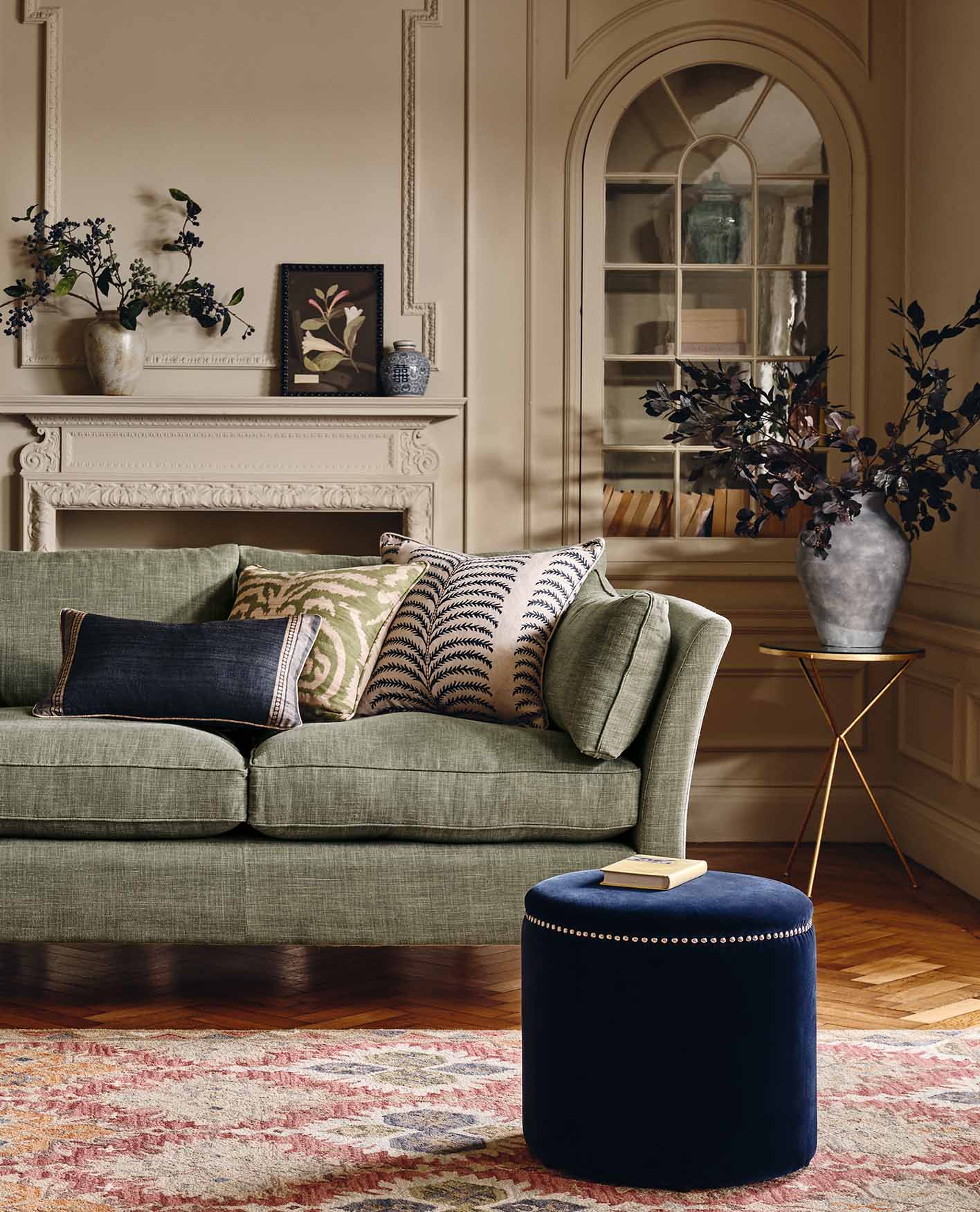 A cosy sitting room with a glass and rattan coffee table, a tan brown leather sofa, a patterned armchair and two lamps. A large window is in the background.
