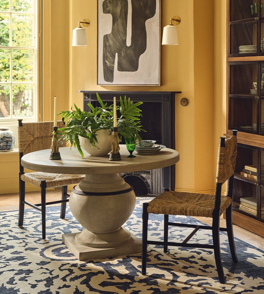 A yellow dining room with plants on the table.