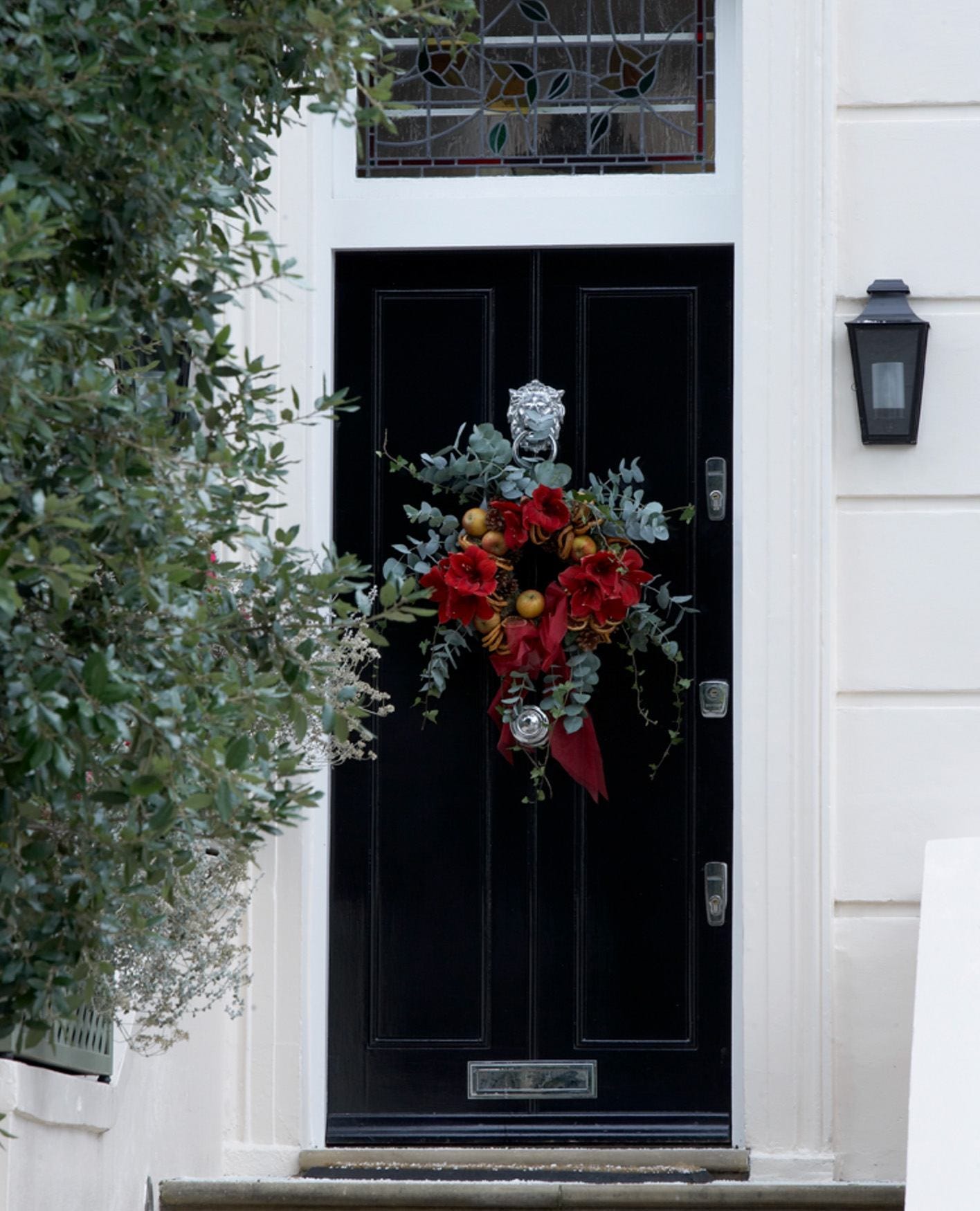 A black doorway decorated with a red and green festive wreath.