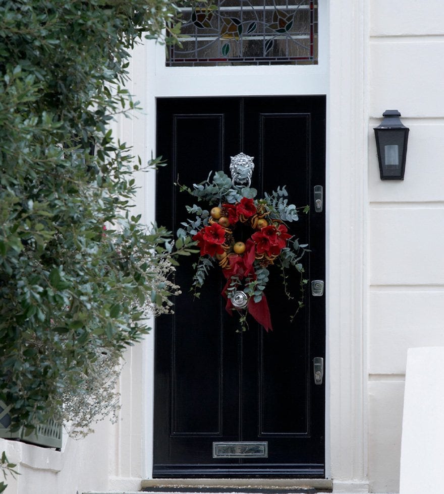 A black doorway decorated with a red and green festive wreath.