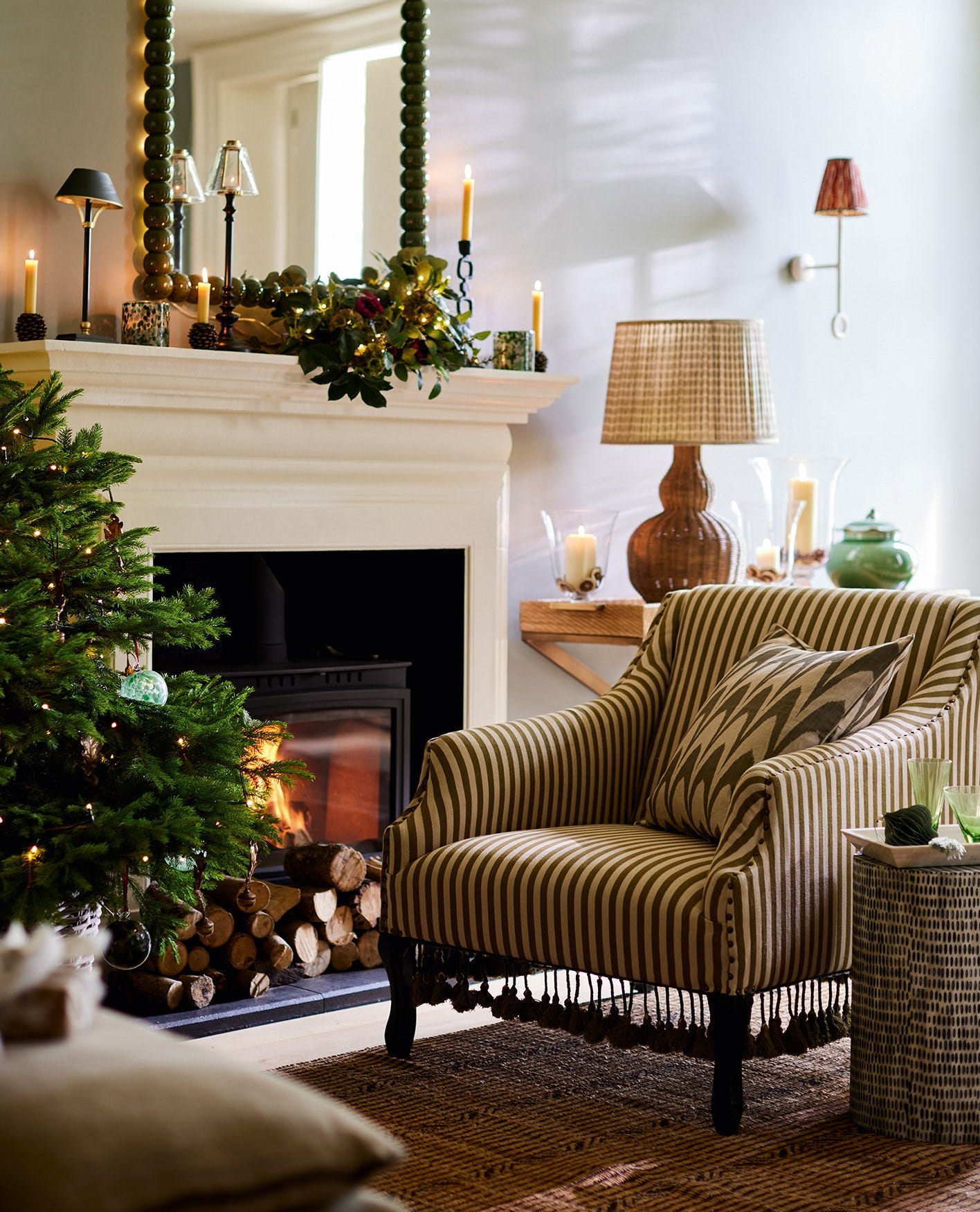 A green-and-white striped armchair sits in front of a roaring fire and a Christmas tree