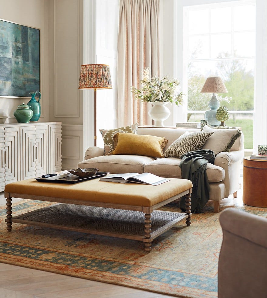 A sitting room decorated with colourful accents, including a yellow upholstered ottoman, blue vases and orange lampshades.