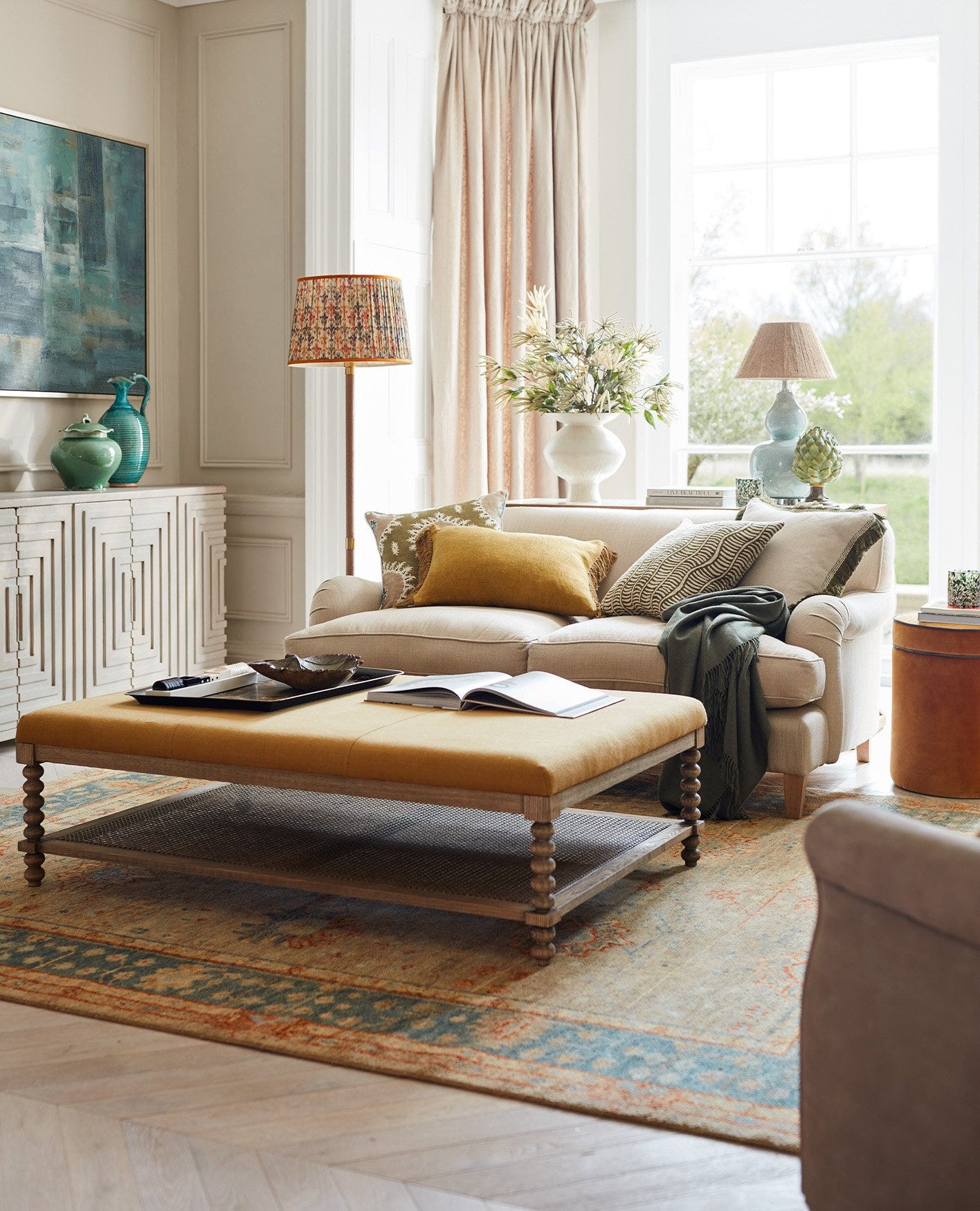 A sitting room decorated with colourful accents, including a yellow upholstered ottoman, blue vases and orange lampshades.