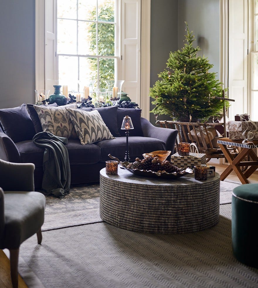 A velvet sofa piled high with pillows sits in a cozy sitting room, with a black-and-white coffee table sits and a Christmas tree decorated with warm string lights.