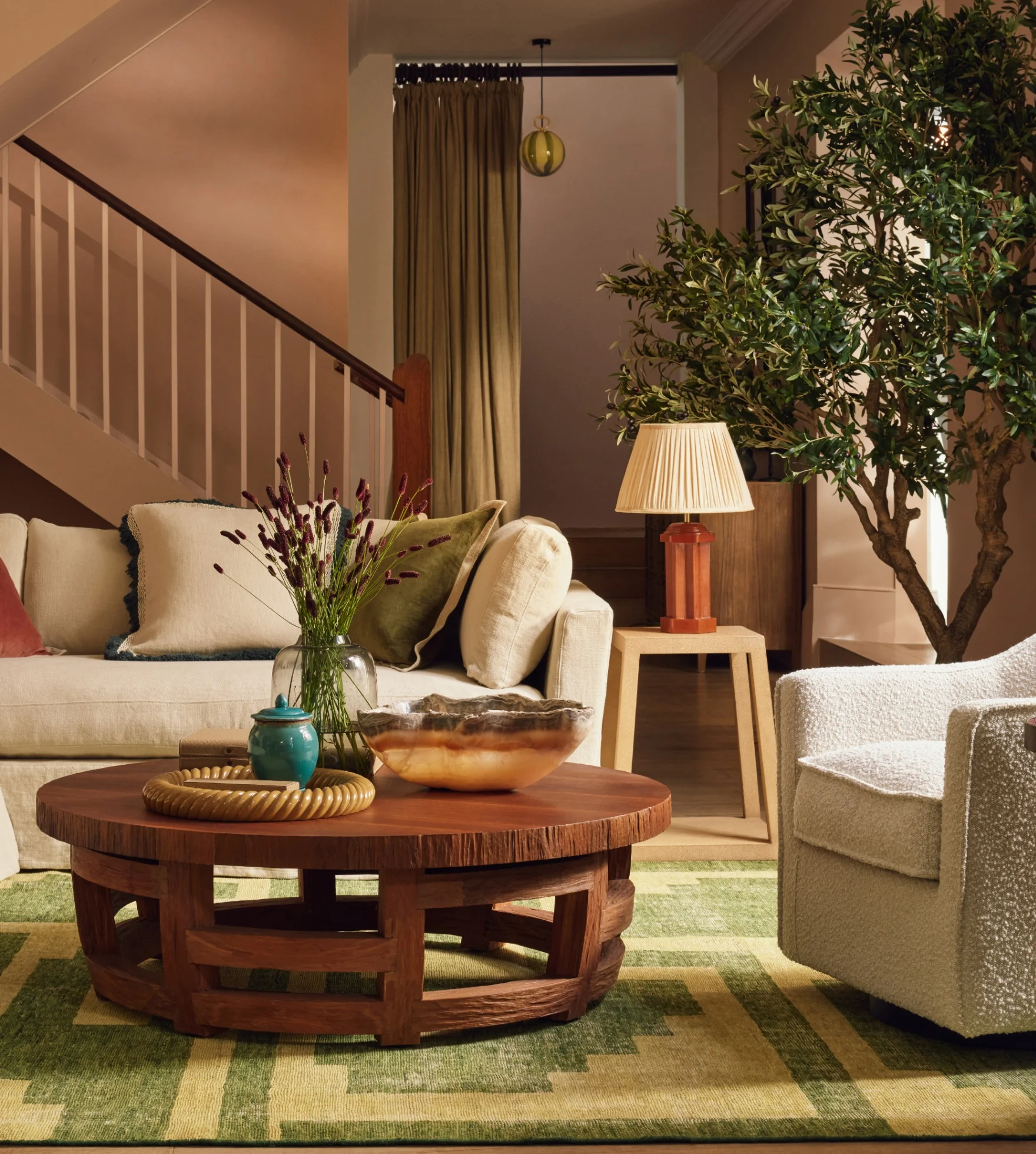 A softly coloured bedroom with a fourposter bed, floral-print red, olive green and cream armchair, bedspread and rug.