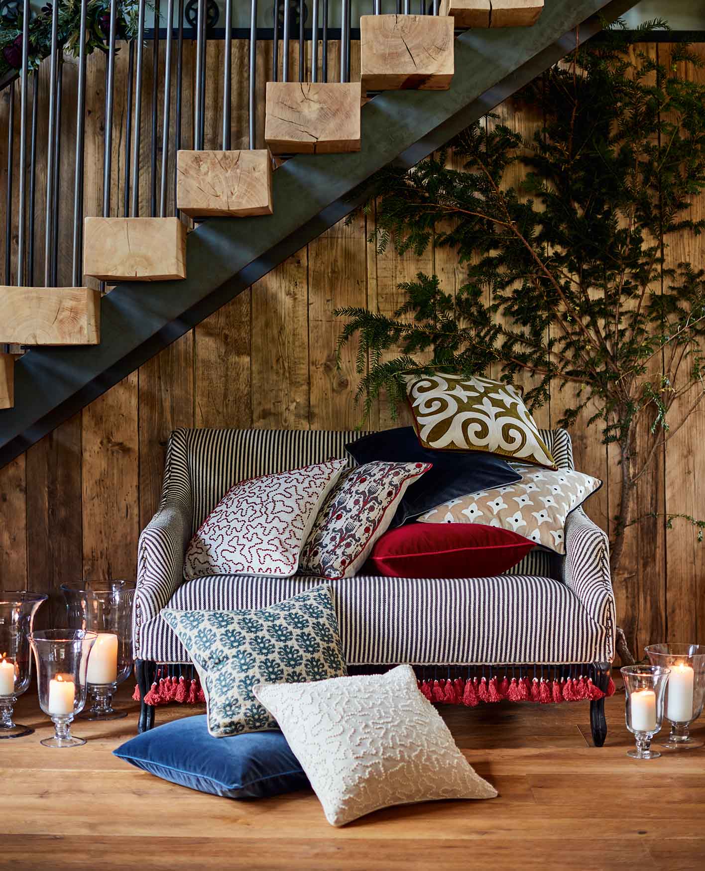 A wooden staircase above a sofa surrounded by cushions and candles.