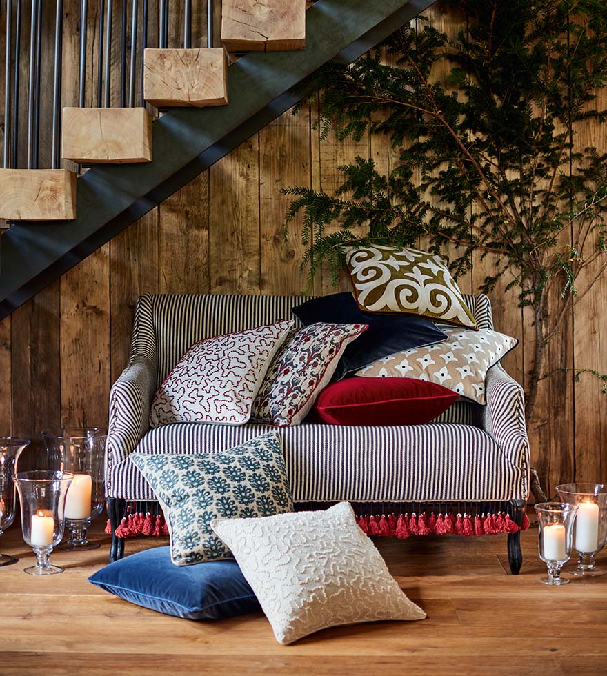 A wooden staircase above a sofa surrounded by cushions and candles.
