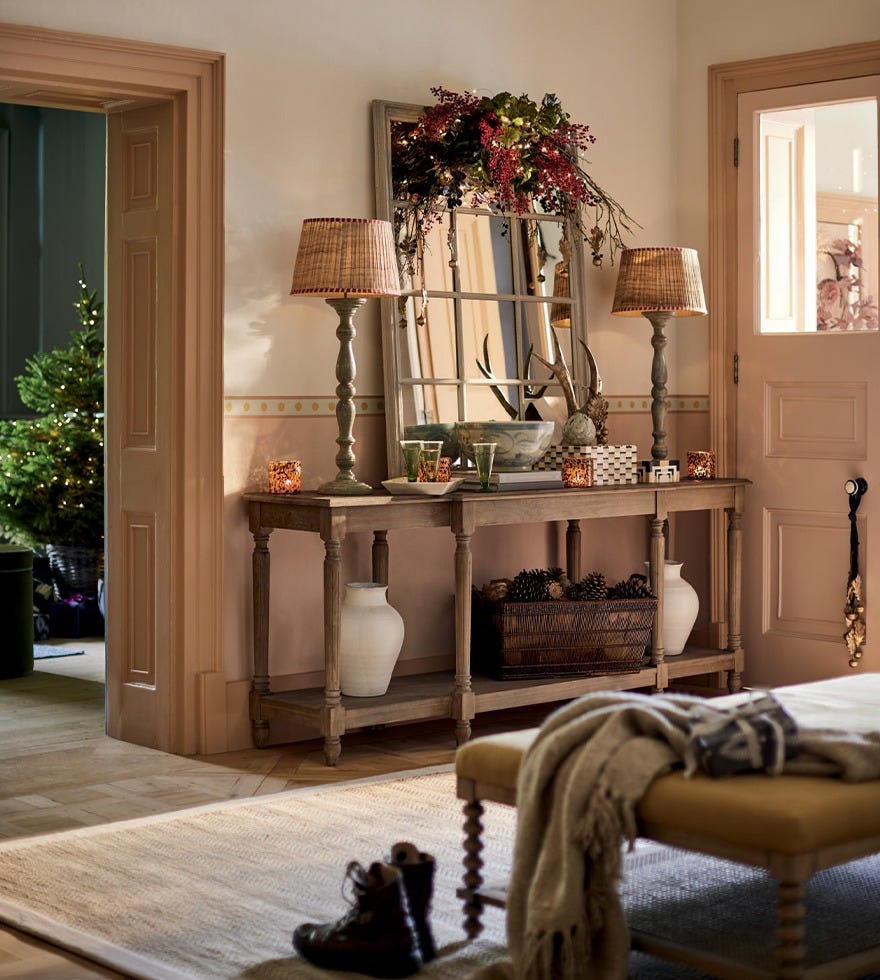 A festive hallway scene featuring a console table decorated with table lamps, a mirror and festive foliage.