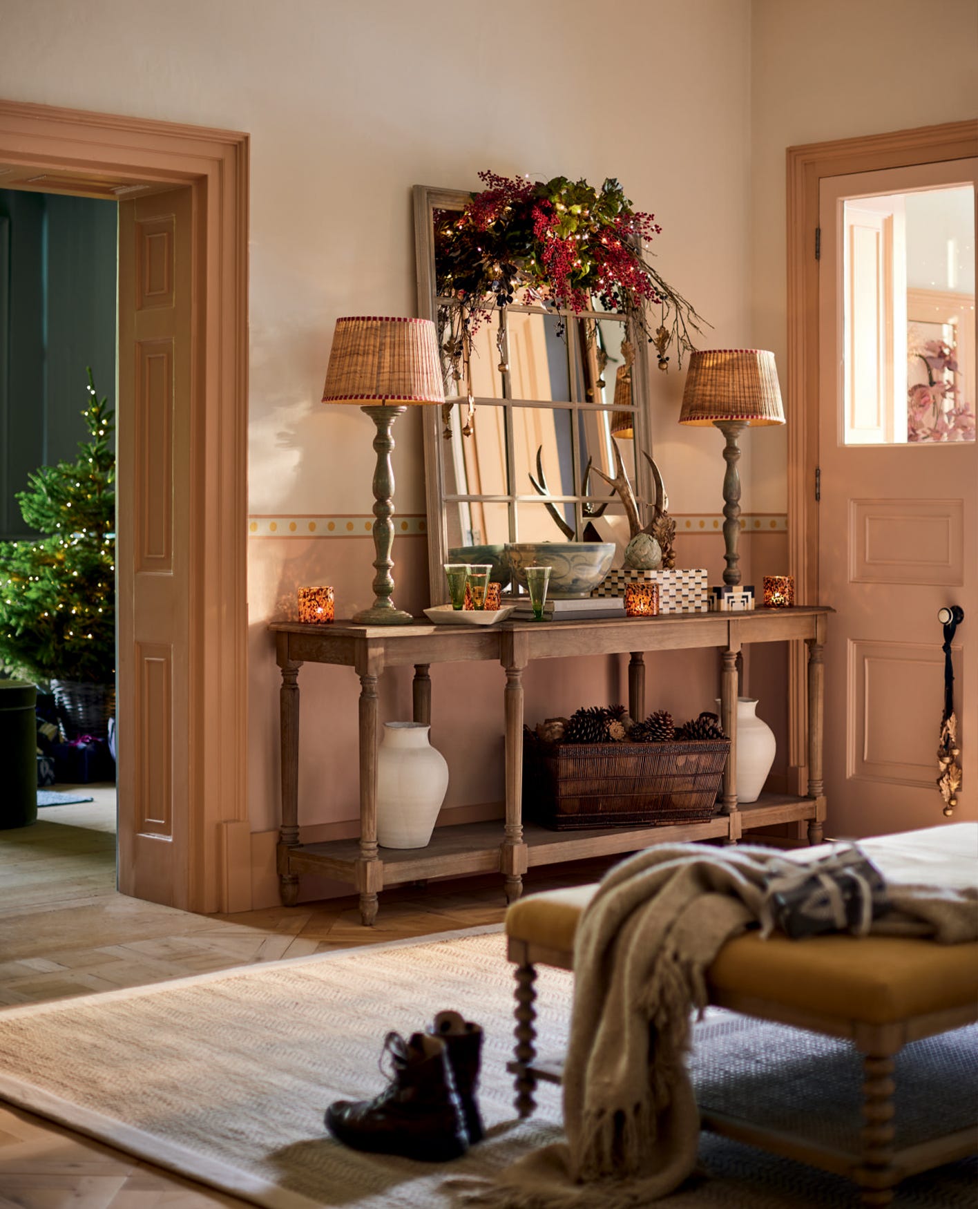 A festive hallway scene featuring a console table decorated with table lamps, a mirror and festive foliage.