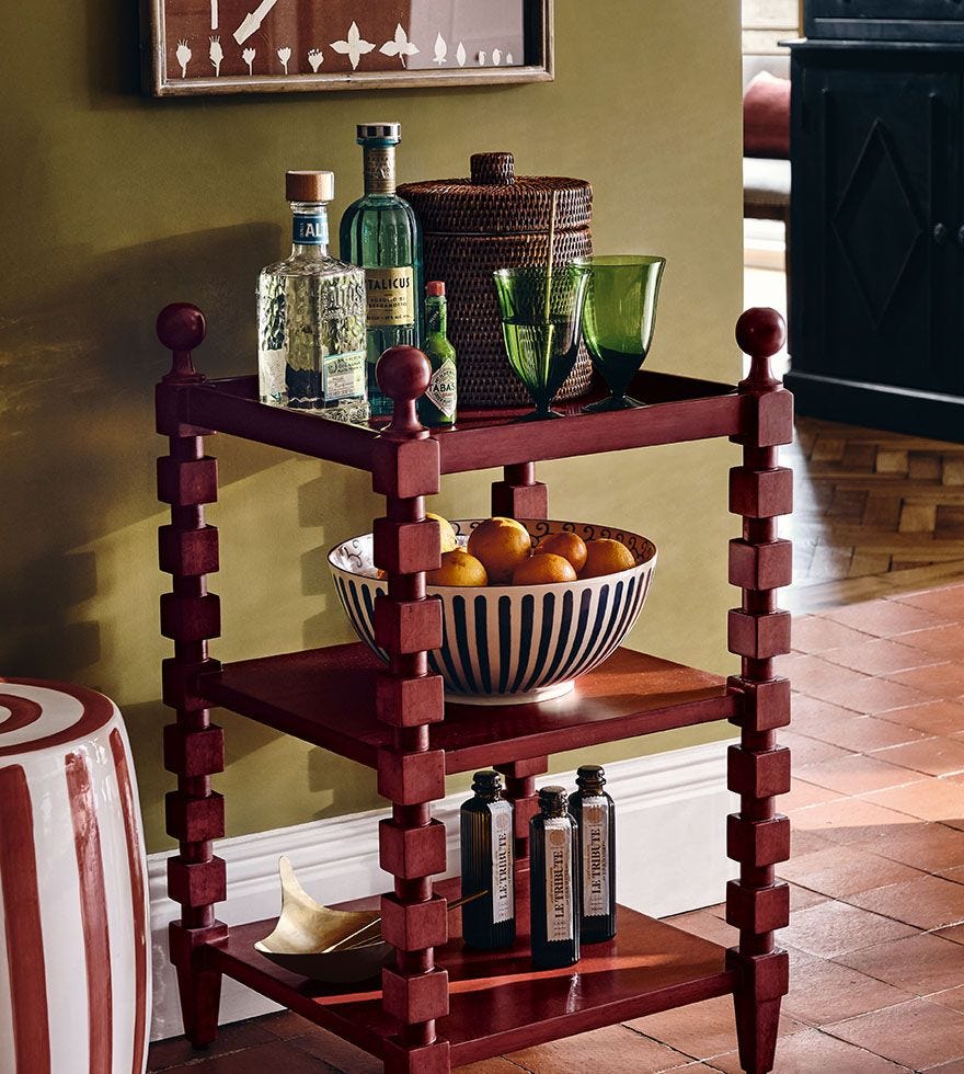 A red side table with cubed, bobbin-inspired legs holds an array of glassware and bottles of drink.