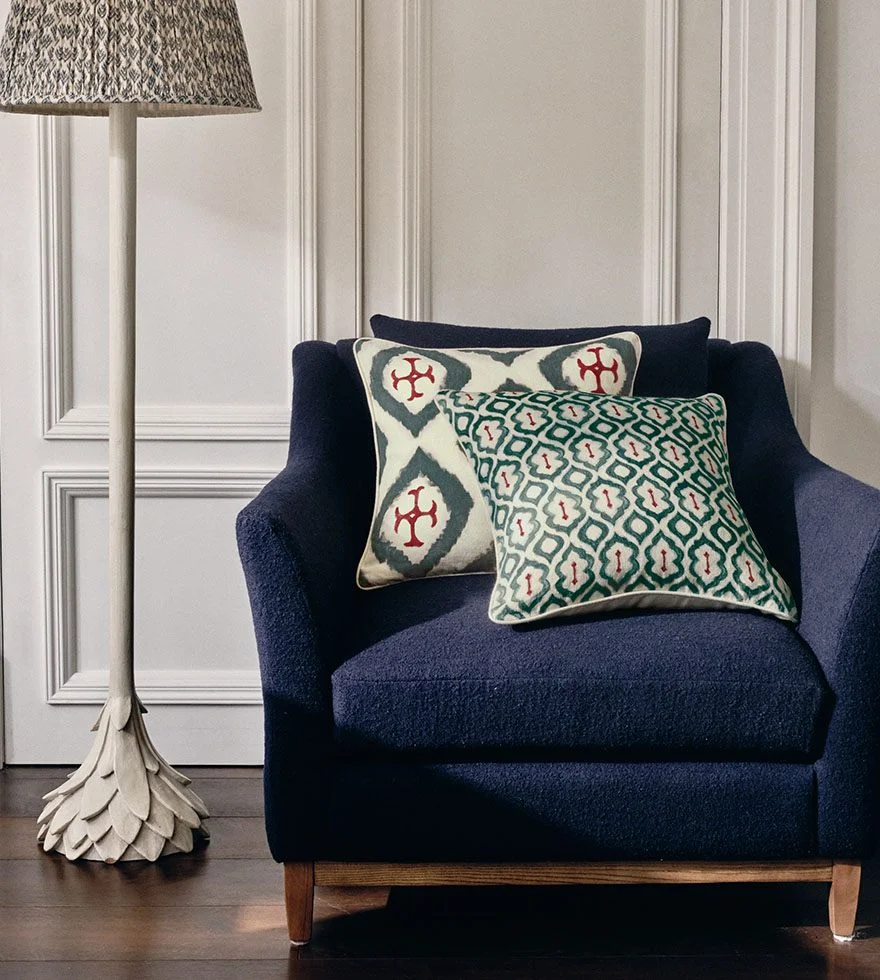 A navy blue armchair, decorated with patterned pillows, sits next to a white floor lamp featuring a patterned shade.