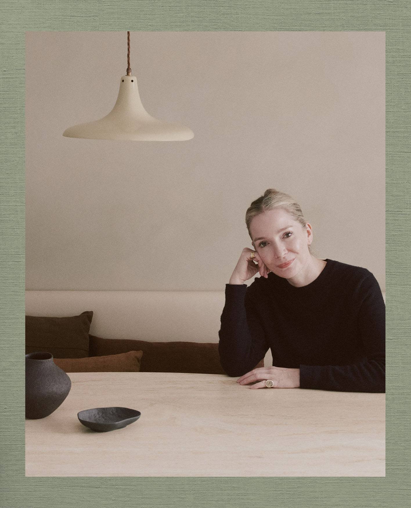 Louisa Grey, wearing a black long-sleeved top, sitting at a wooden table.