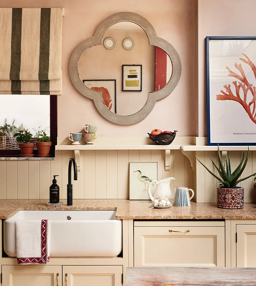 A kitchen sink is surrounded by shelving, artwork, mirrors, plants and homeware.