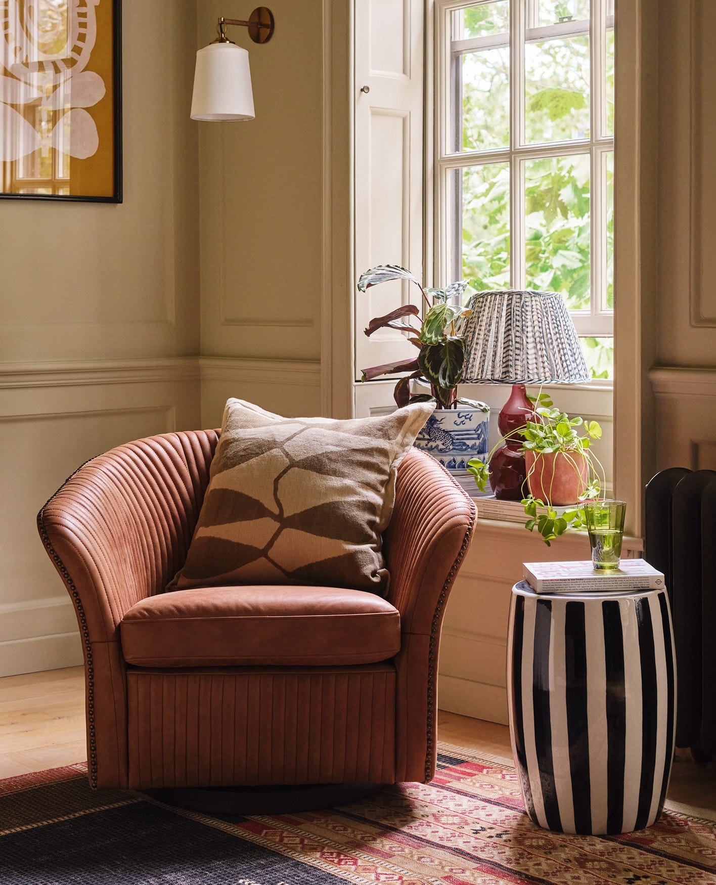 A leather armchair decorated with a beige cushion and sitting next to a striped ceramic stool