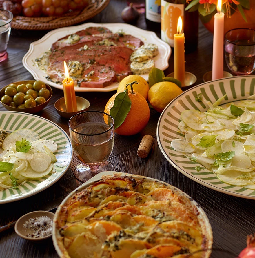 An array of dishes on green striped tableware, decorated with candles, fruit and glassware.