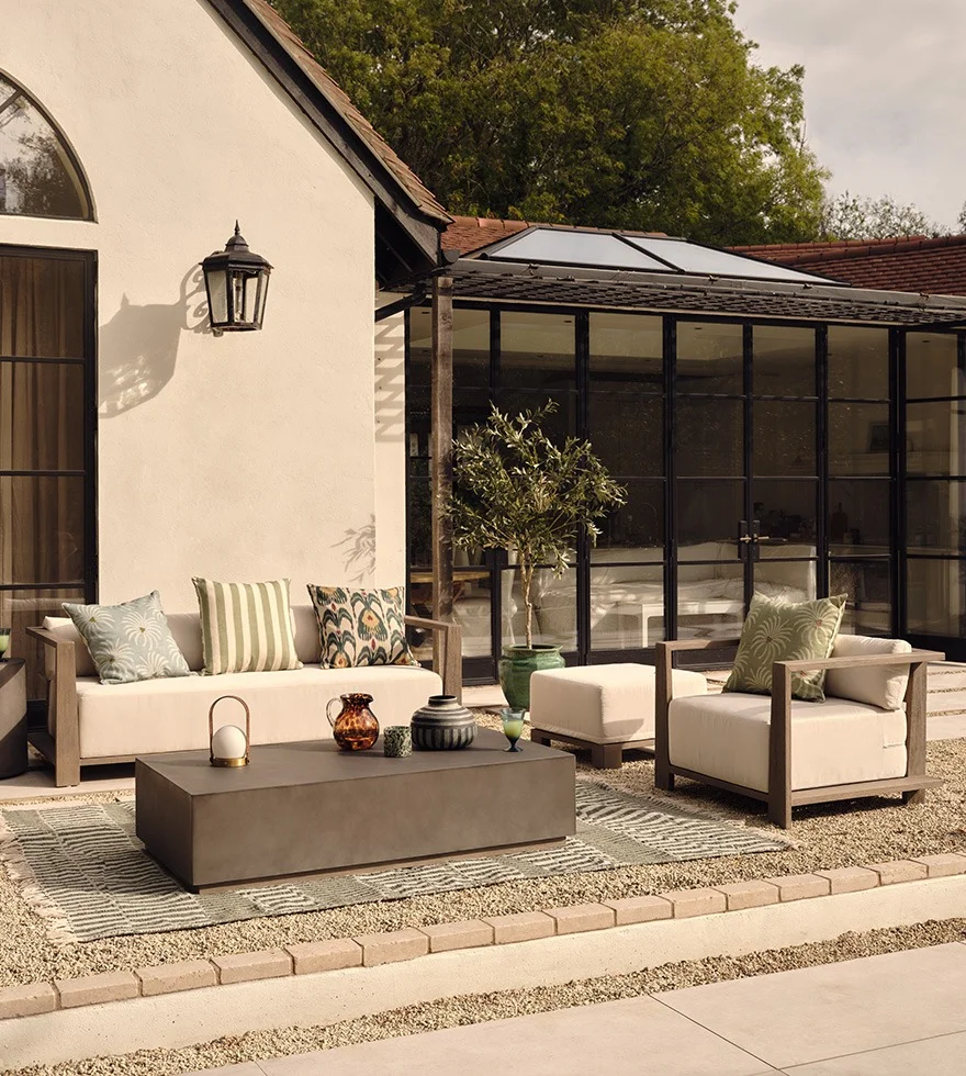 An outdoor lounge area including a sofa and armchair, coffee table, outdoor rug and decor.