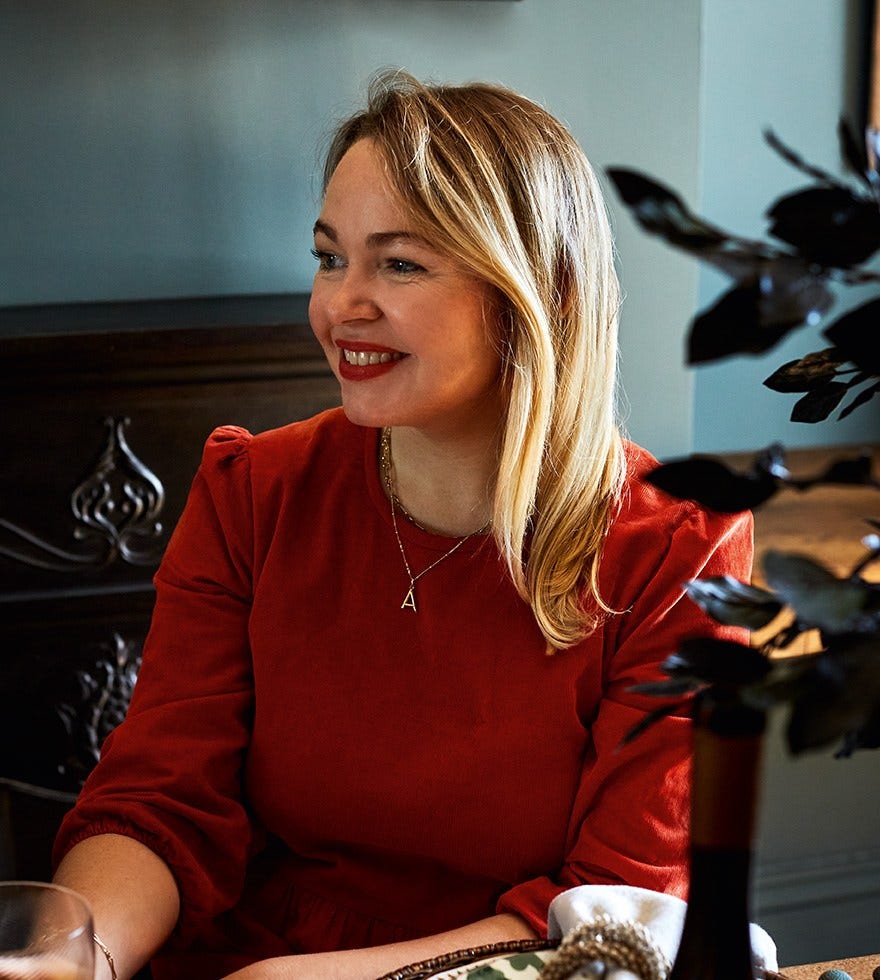 Rosie Birkett wears a red velvet dress and is smiling to someone off camera