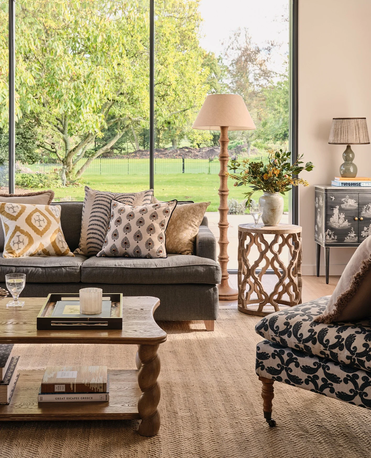 A navy sofa, pattern upholstered chairs and a wooden coffee table are arranged in front of floor-to-ceiling glass windows.