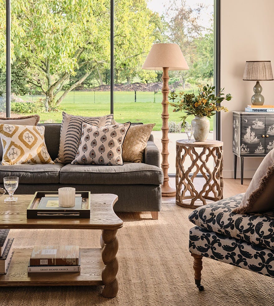 A navy sofa, pattern upholstered chairs and a wooden coffee table are arranged in front of floor-to-ceiling glass windows.