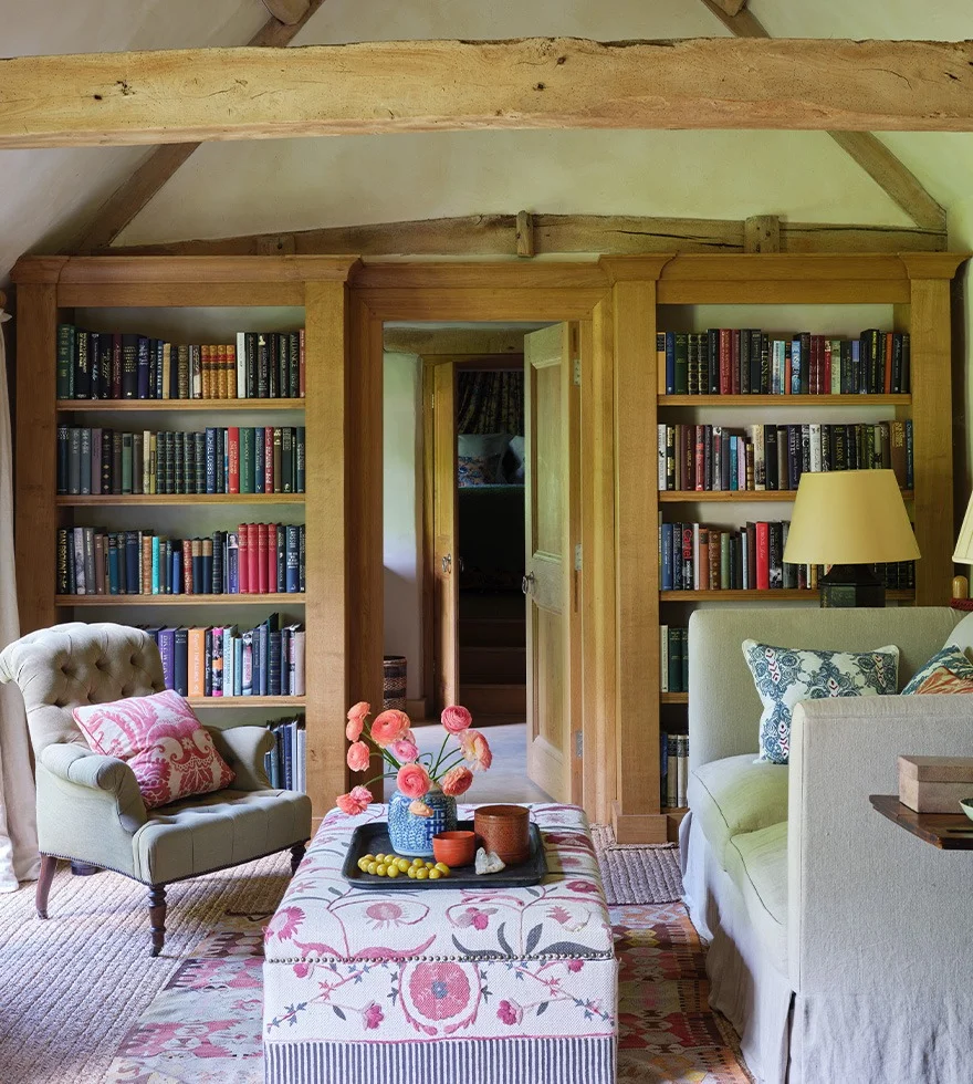 A cottage style sitting room featuring a bookcase, sofa, armchair and an ottoman