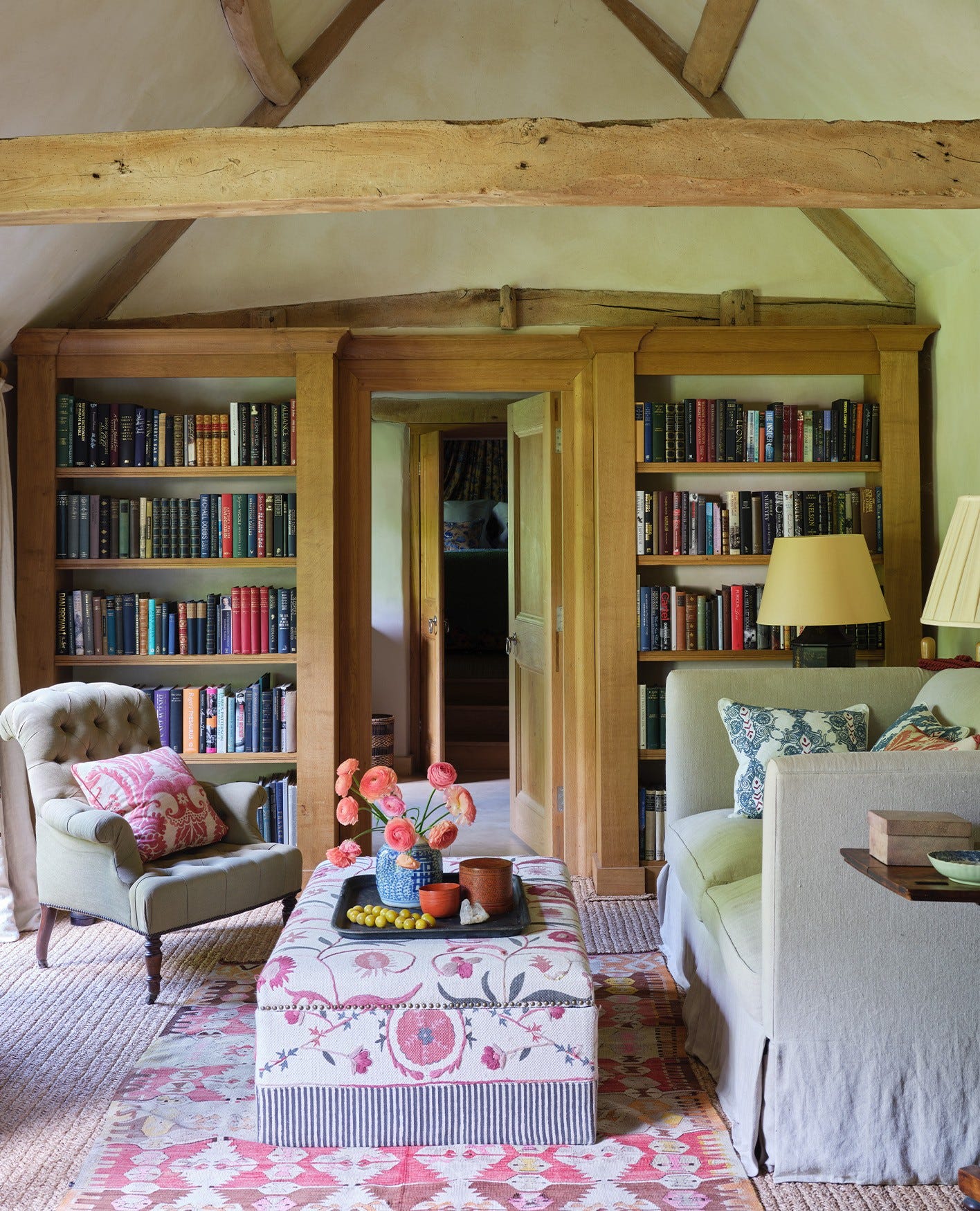 A cottage style sitting room featuring a bookcase, sofa, armchair and an ottoman